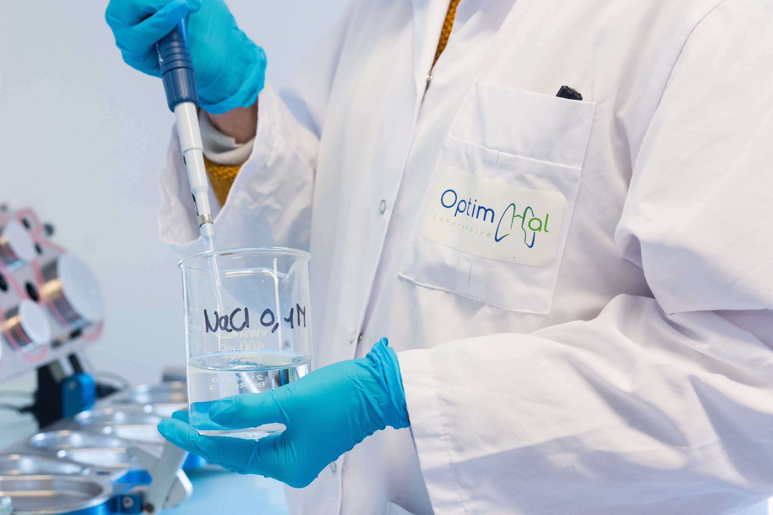 Des mains avec des gants de laboratoire tenant un récipient et une pipette